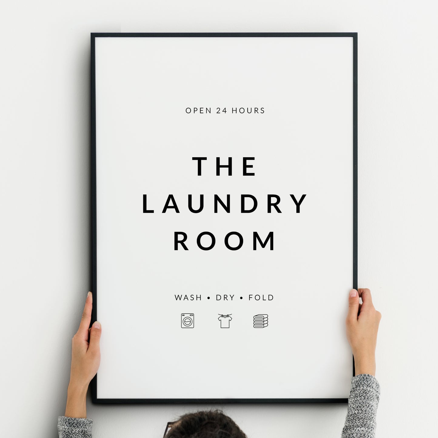 Single portrait print. Text reads: Open 24 Hours The Laundry Room Wash Dry Fold. Small icons representing wash, fold, and dry are below the text. Text is in an upper case sans serif font, black on a white background. Styling is modern and minimalist.