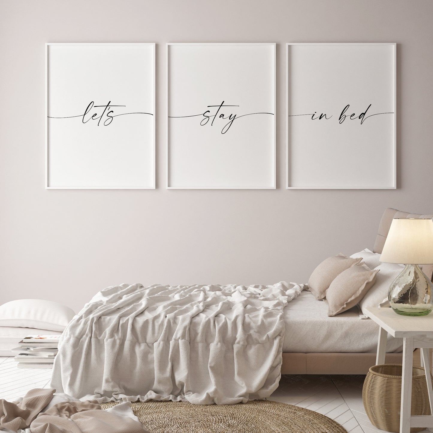 Set of 3 portrait typography prints positioned side by side on a bedroom gallery wall. The prints feature the quote "let's stay in bed", which is split across the 3 prints. All text is in a stylish script font, with the leading and trailing edged of the text on each print stretching out to the outer edges of the respective prints. Text is black on a white background.