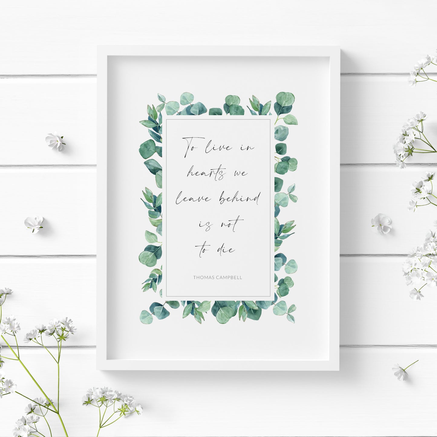 Single portrait print featuring the quote "To live in hearts we leave behind is not to die" with an attribution to Thomas Campbell. Text is black on a white background and within a rectangular border of eucalyptus leaves.