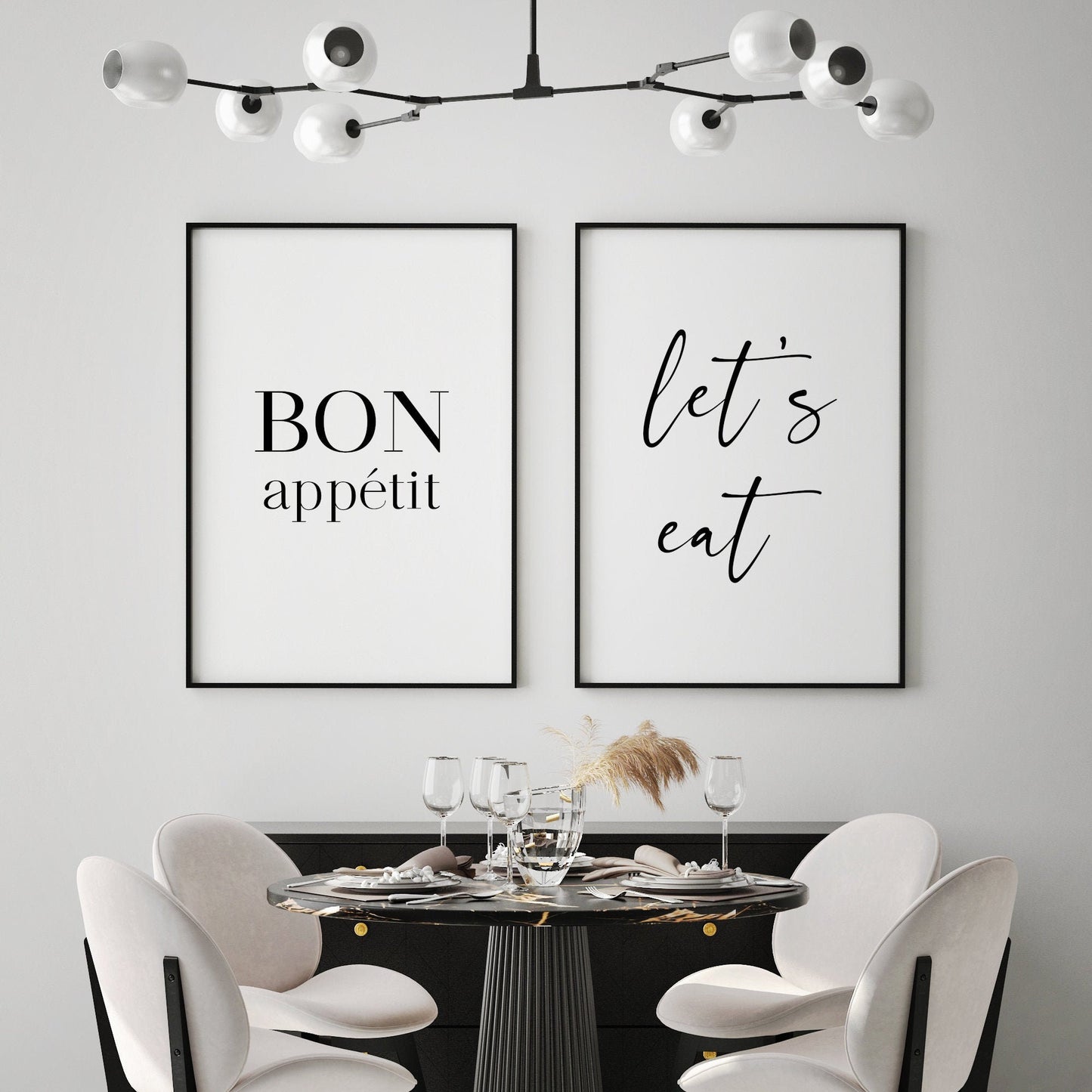 Set of 2 portrait typography prints. Print 1 reads "Bon appetit" in a formal serif font. The word "Bon" is in upper case and the word "appetit" is positioned below in lower case, sized so the width of both words is the same. Print 2 reads "let's eat" in a complementary script font, all in lower case. All text is black on a white background.