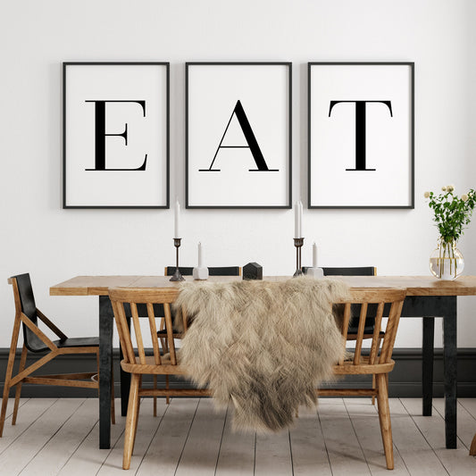 Set of 3 portrait typography prints. The word EAT in all caps is spread across the 3, with one letter on each print. Text is black on a white background, with a formal serif font used. The perfect statement kitchen or dining room wall art.