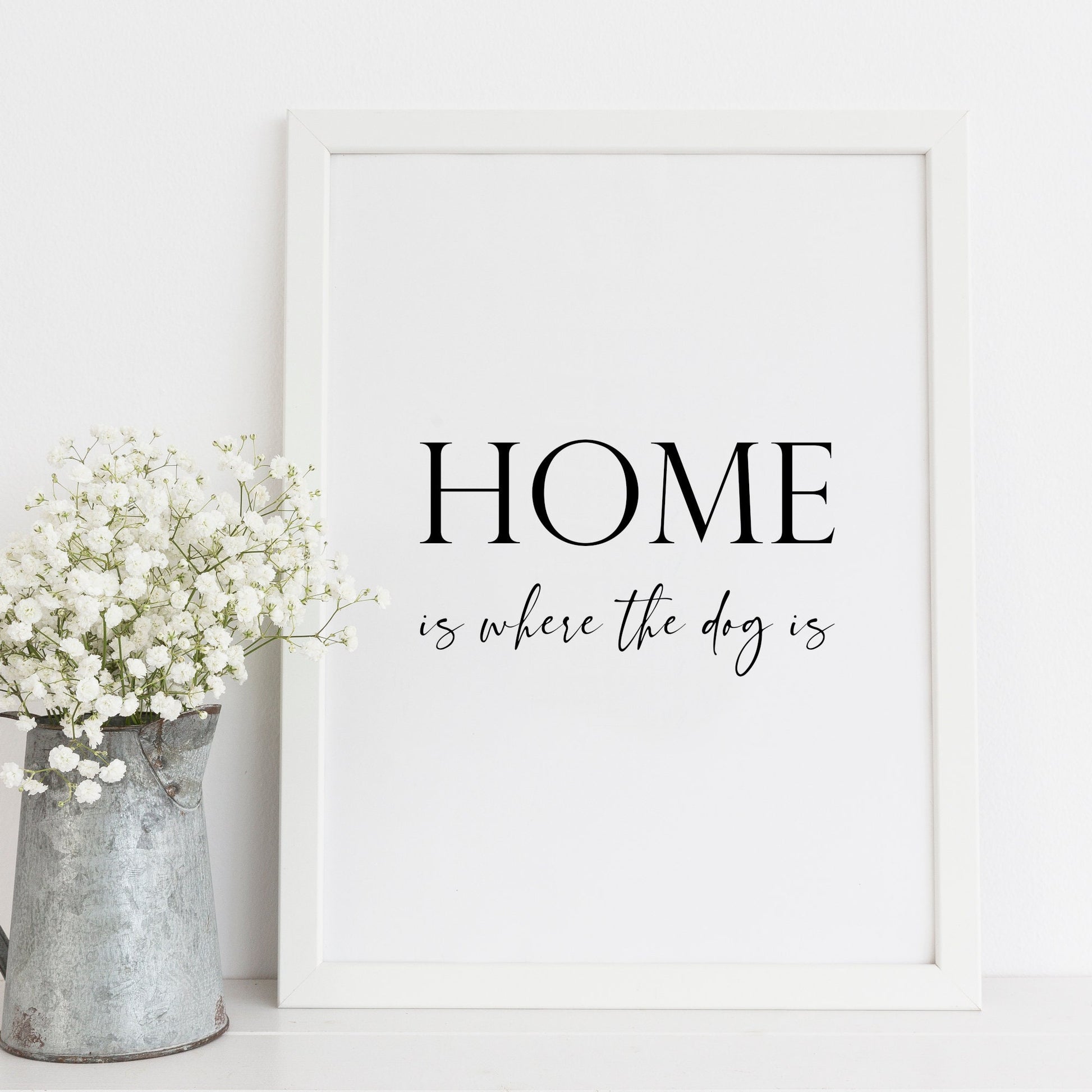 Single portrait typography print. Quote reads: Home is where the dog is. The word home is positioned prominently in an upper case serif font, with the remaining text placed below in a stylish script font. Text is black on a white background.