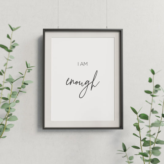 Single portrait print displayed in a black frame. Its minimalist style shows black text on a white background with text that reads I am enough. The word enough is displayed prominently in an elegant script font.