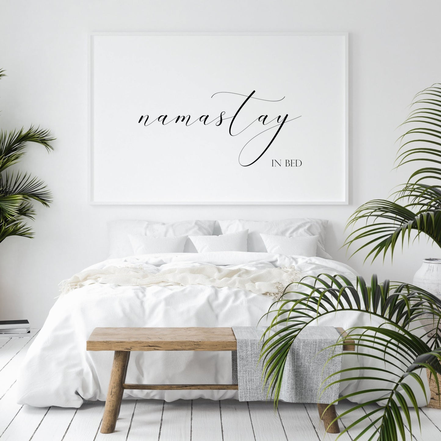 Single landscape typography print. Text reads: namastay in bed. The word namastay is positioned prominently in an elegant script font, with the remaining text in a small upper case serif font aligned to its bottom right. Text is black on a white background.