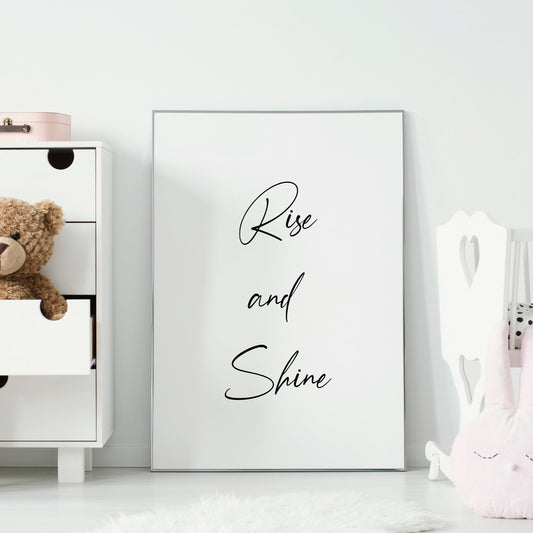 Single portrait typography print shown in a nursery setting. Text reads: rise and shine. The text is black on a white background and is shown in a bold and elegant script font.