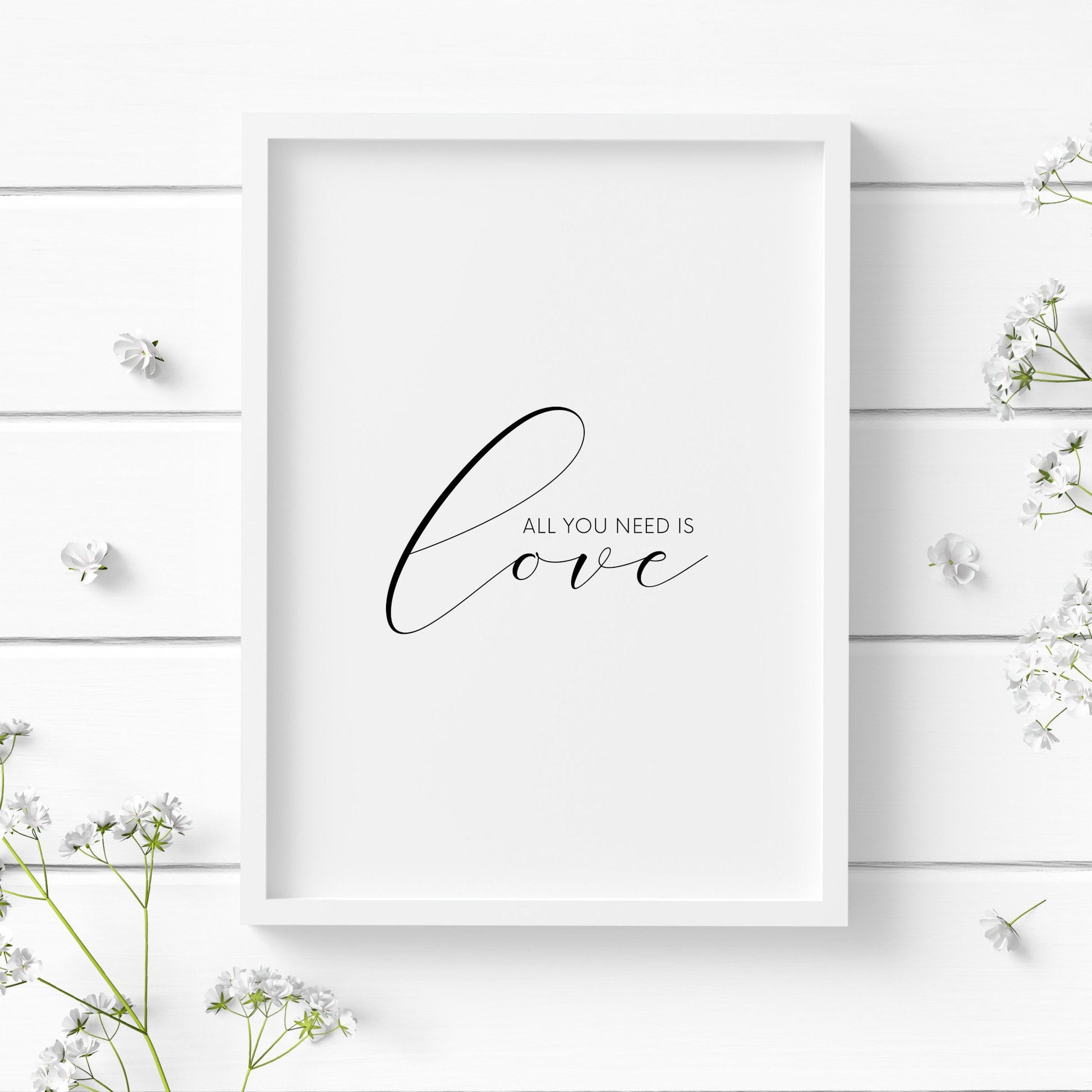 Single portrait typography print. Text reads: All you need is love. The word "love" is positioned prominently in an elegant script font. Text is black on a white background. It makes the perfect Valentine's Day gift.