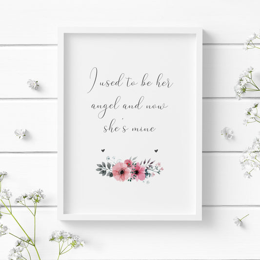 A single portrait print shown in a white frame. Text reads: I used to be her angel and now she's mine. The text is in a delicate script font, with a tasteful floral ornament below in pink, and two small grey hearts left and right.