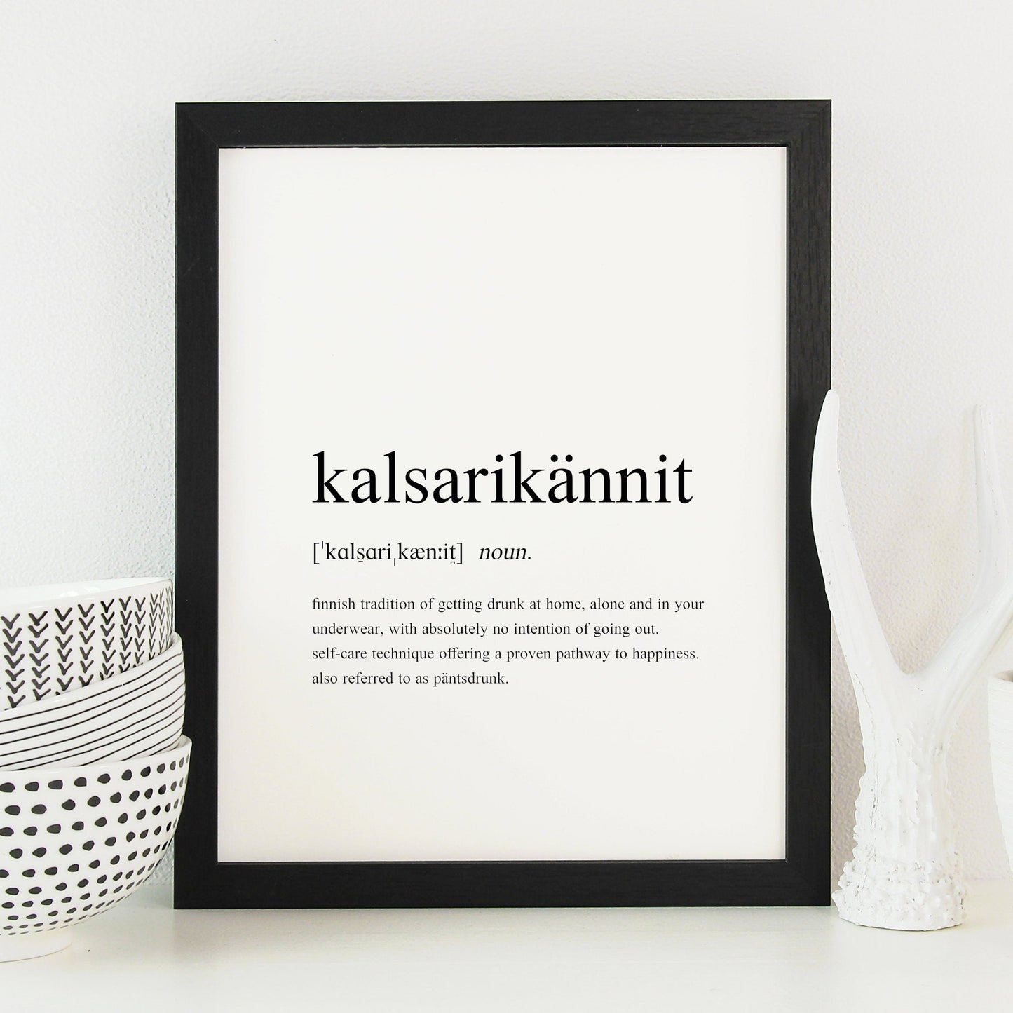 A single portrait typography print in a traditional dictionary style, showing a humorous definition of the Finnish word Kalsarikännit. The word, it&#39;s pronunciation and definition are listed. Text is black on a white background.